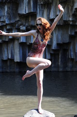 A young girl in a swimsuit standing on a stone in the middle of a mountain lake