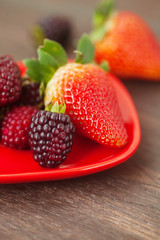 red juicy strawberry and blackberry in red plate on a wooden sur