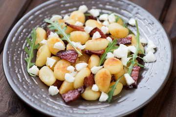 Roasted gnocchi with cheese, meat and arugula in a glass plate