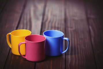 Three color cups on woodent table.