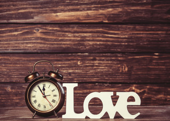 Clock with word love on wooden table.