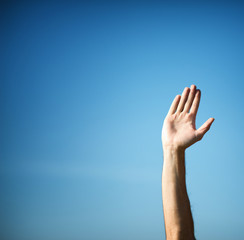 Raising hand with hand palm against blue sky