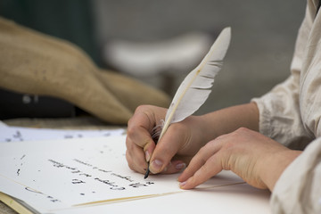 hands writing a letter with a plume