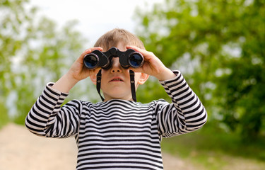 Little boy scanning the woods with binoculars