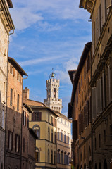 Narrow streets and old buildings in Siena, clock tower in back