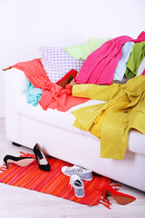 Messy colorful clothing on  sofa on light background