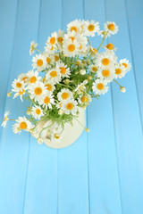 Chamomiles in jug  on color wooden background