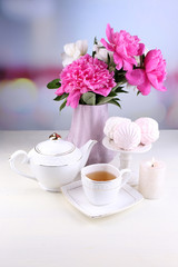 Composition of beautiful peonies in vase, tea in cup and