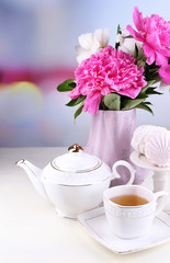Composition of beautiful peonies in vase, tea in cup and