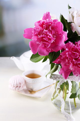 Composition of beautiful peonies in vase, tea in cup and