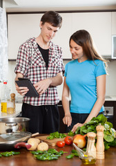 Happy couple cooking with electronic Book in kitchen