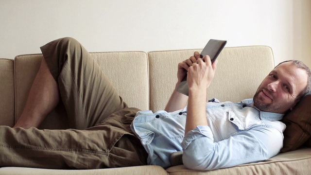 Young happy man with tablet computer on sofa at home