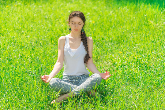 Young woman sitting in a lotus position on a green lawn.