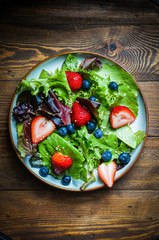 Green salad with berries on wooden background