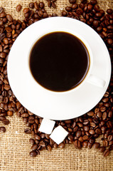 Cup of coffee with refined sugar and coffee beans.