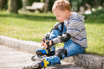 Little boy lace his roller skate sitting on the sidewalk