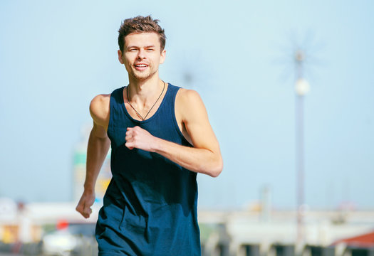 Young man jogging at the street in summer morning time