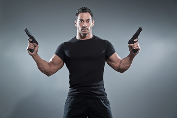 Action hero muscled man holding two guns. Wearing black t-shirt