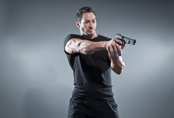Fototapeta na wymiar Action hero muscled man shooting with gun. Wearing black t-shirt
