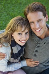 Fototapeta premium Cute couple sitting in the park embracing smiling at camera
