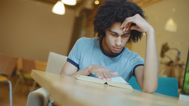 Attractive young man reading a book, he holds his head