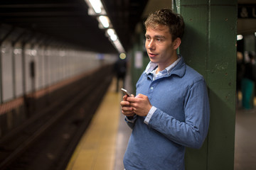 Young caucasian man texting on cellphone subway