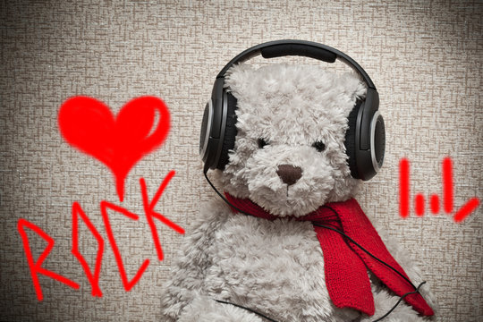 Toy teddy bear with a red scarf listening to music on headphones