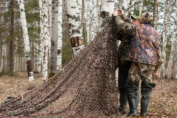 two hunters pull camouflage netting