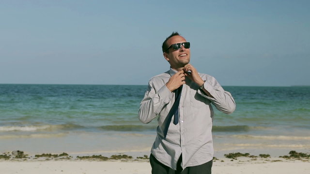Happy businessman taking off his clothes on the beach