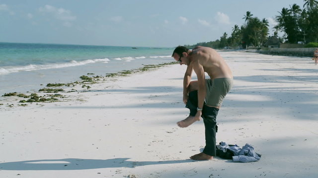 Businessman taking off his trousers on the beach, steadycam shot