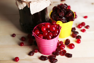 Fresh and dry cranberry in pails on wooden table close-up