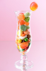 Different colorful fruit candy in glass on pink background