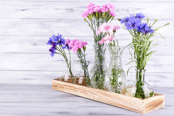 Beautiful summer flowers in vases on grey wooden background