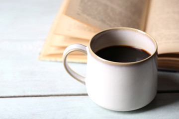 Cup with hot coffee and old book on wooden background