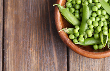 Green peas in wooden bowl on wooden background