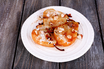 Baked pears with syrup on plate, on color wooden background