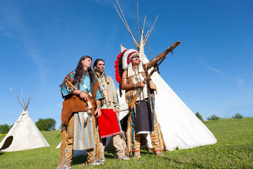 Three North American Indians stand near a wigwam