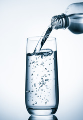 Pouring water into glass  from bottle on blue background