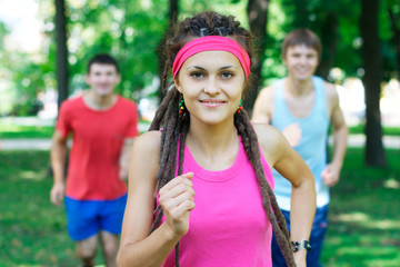 Smiling girl jogging with two guys on the background at the park