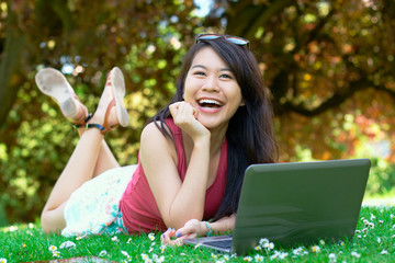 Smiling asian girl with a laptop at the park