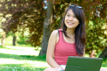 Smiling asian girl with a laptop at the park