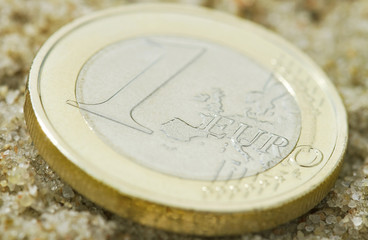 Euro coin on sand.