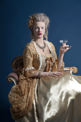 Retro baroque fashion woman wearing gold dress. Holding wine gla