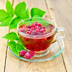 Tea with raspberries in glass cup on board