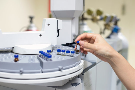 scientist hand holding an amber vial, Vials in the autosampler tray. Chemistry lab