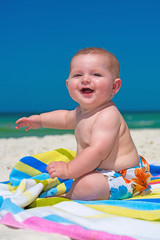 Happy infant baby boy sitting on towel at the beach