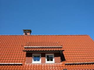 Mansarde und Dachgaube mit weißen Fenstern auf einem rotbraunen Ziegeldach vor blauem Himmel im...