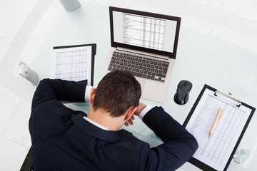 Fototapeta na wymiar Tired Businessman Sleeping While Calculating Expenses In Office