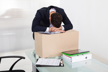 Tired Businessman Resting On Cardboard Box At Desk
