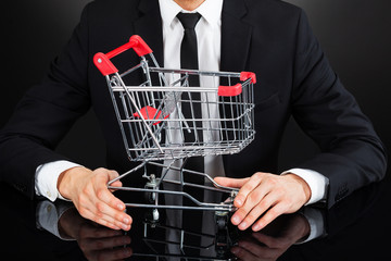 Businessman Holding Shopping Cart Model At Desk